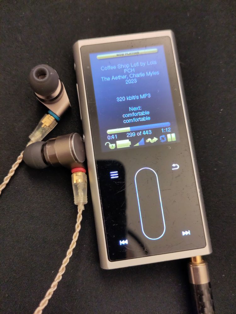 A picture of a Fiio M3K running Rockbox, next to two IEM earphones